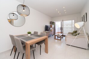 A modern living room with a wooden dining table, grey chairs, a sofa, and a floor lamp.