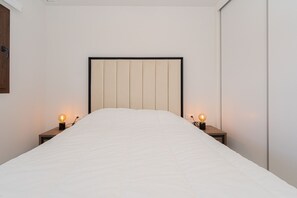 A neatly made bed with a headboard, two bedside tables with lamps, and a wooden door.