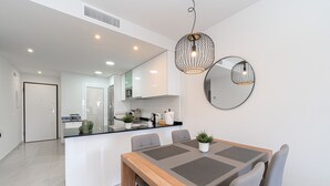 A modern kitchen with white cabinets, a central island, and a dining area with a wooden table and grey chairs. - Apartamento Vamos (Mar de Pulpi) (San Juan de los terreros)