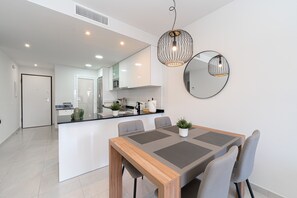 A modern kitchen with white cabinets, a central island, and a dining area with a wooden table and grey chairs. - Apartamento Vamos (Mar de Pulpi) (San Juan de los terreros)
