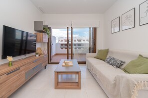 A modern living room with a flat-screen TV, wooden furniture, a coffee table, and a sofa with green cushions.