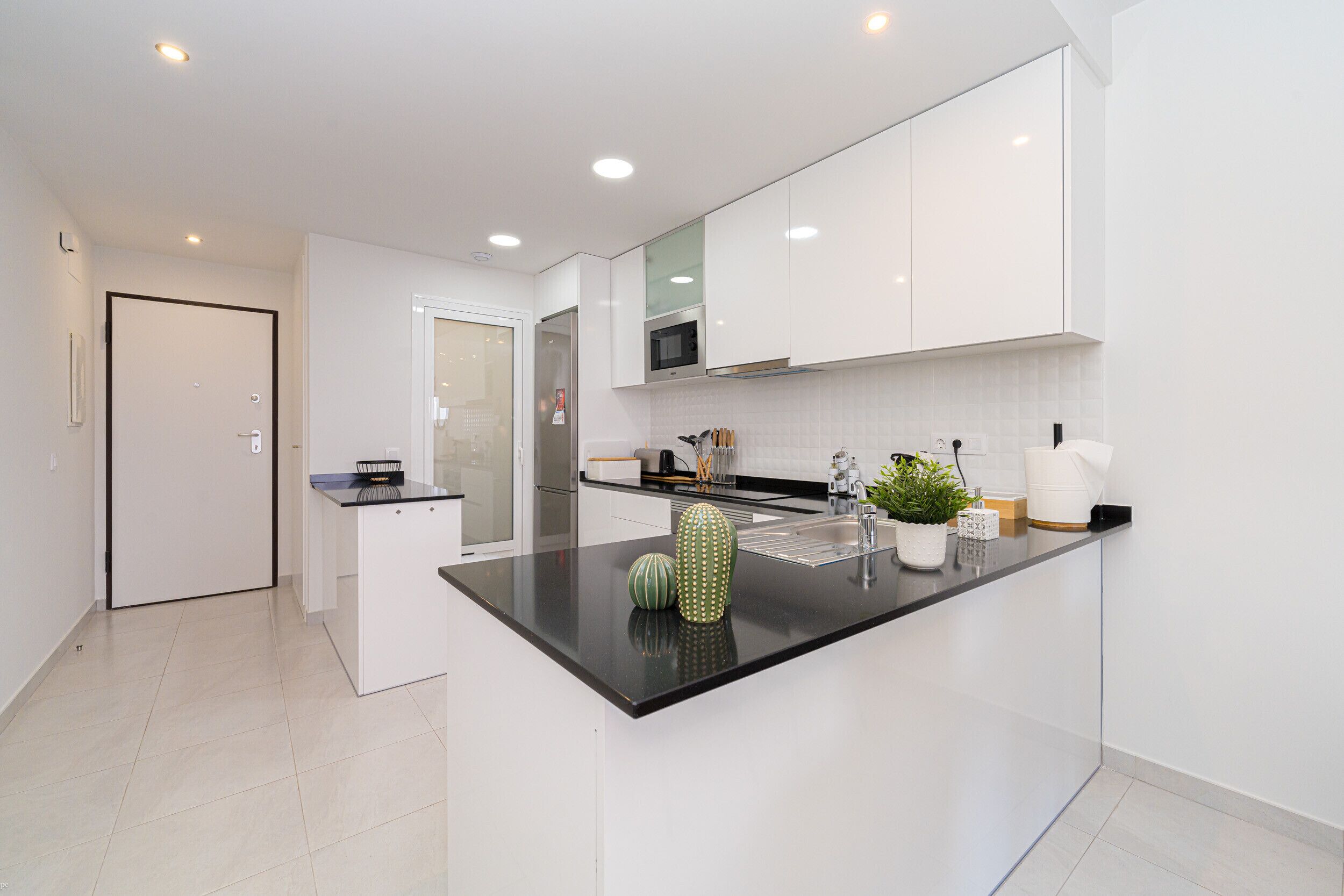 Una cocina moderna con armarios blancos, una encimera negra y un microondas. Hay dos jarrones decorativos sobre la encimera.