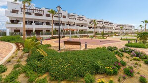 Un hotel de varios pisos con balcones, un patio central con bancos y un jardín bien cuidado.