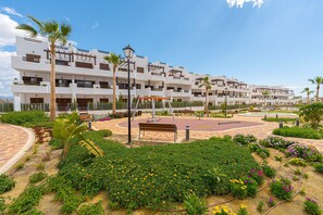 Un hotel de varios pisos con balcones, un patio central con bancos y un jardín bien cuidado.