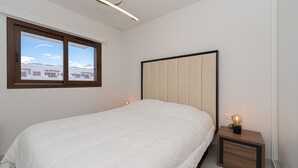 Un dormitorio con cama, mesita de noche, ventana y lámpara de techo.