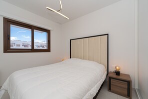 Un dormitorio con cama, mesita de noche, ventana y lámpara de techo.