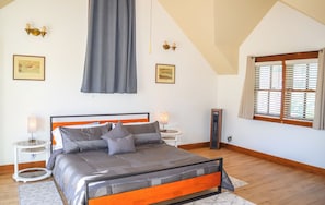 Ein Schlafzimmer mit einem Bett, Nachttischlampen, einer Heizung, einem Fenster mit Jalousien und Kunstwerken an den Wänden.