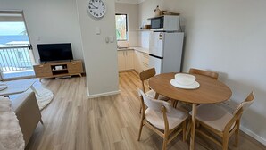 Un apartamento moderno con sala de estar, cocina y comedor. Incluye televisión, microondas, refrigerador y una mesa de comedor con sillas.