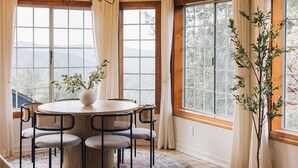 Et spiseområde med et rundt bord, seks stole, en vase med blomster og en lysekrone.