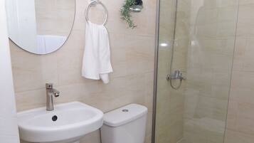 Baño con lavabo, inodoro y ducha con mampara de vidrio.