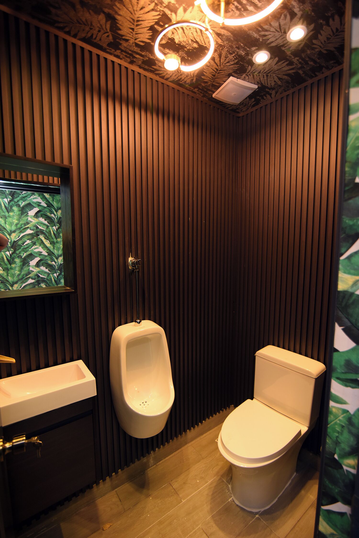 A modern bathroom with vertical wooden paneling, a urinal, a toilet, and a sink.