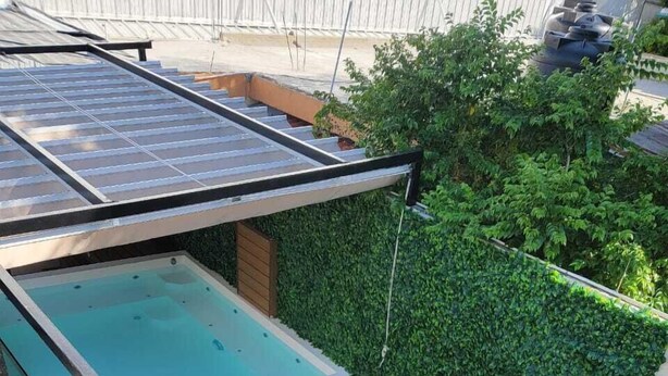 Ein Poolbereich auf dem Dach mit Glasumrandung, Holzterrasse und einer Hecke als Wand.