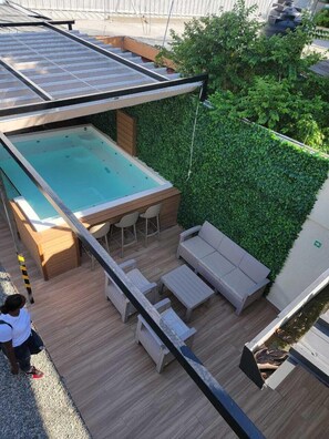 A rooftop pool area with a glass enclosure, wooden deck, and a green hedge wall. - solmirooms (Santo Domingo Este)