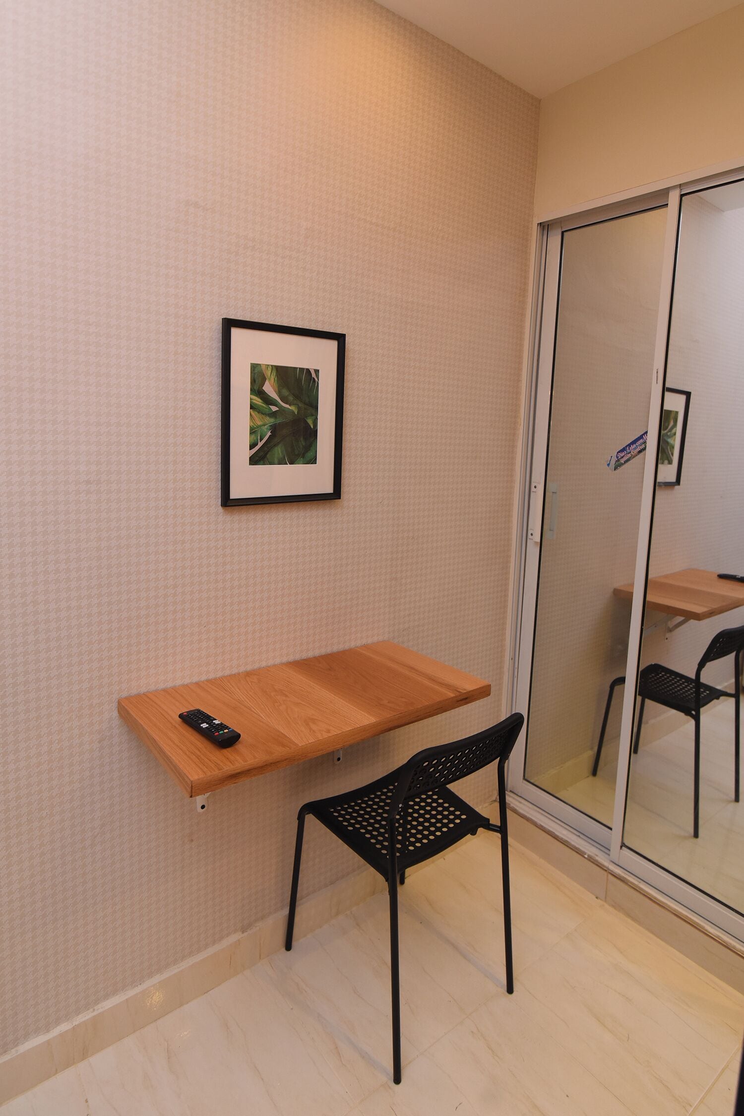 Ein kleiner Raum mit einem Holztisch, einem schwarzen Stuhl und einem gerahmten Bild an der Wand.