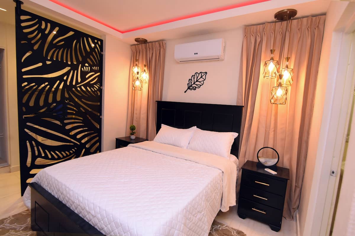 A bedroom with a bed, a nightstand, an air conditioner, and decorative wall art.