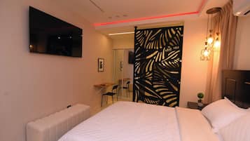 A modern hotel room with a large bed, a flat-screen TV mounted on the wall, a small desk with a chair, and a decorative partition with leaf patterns.
