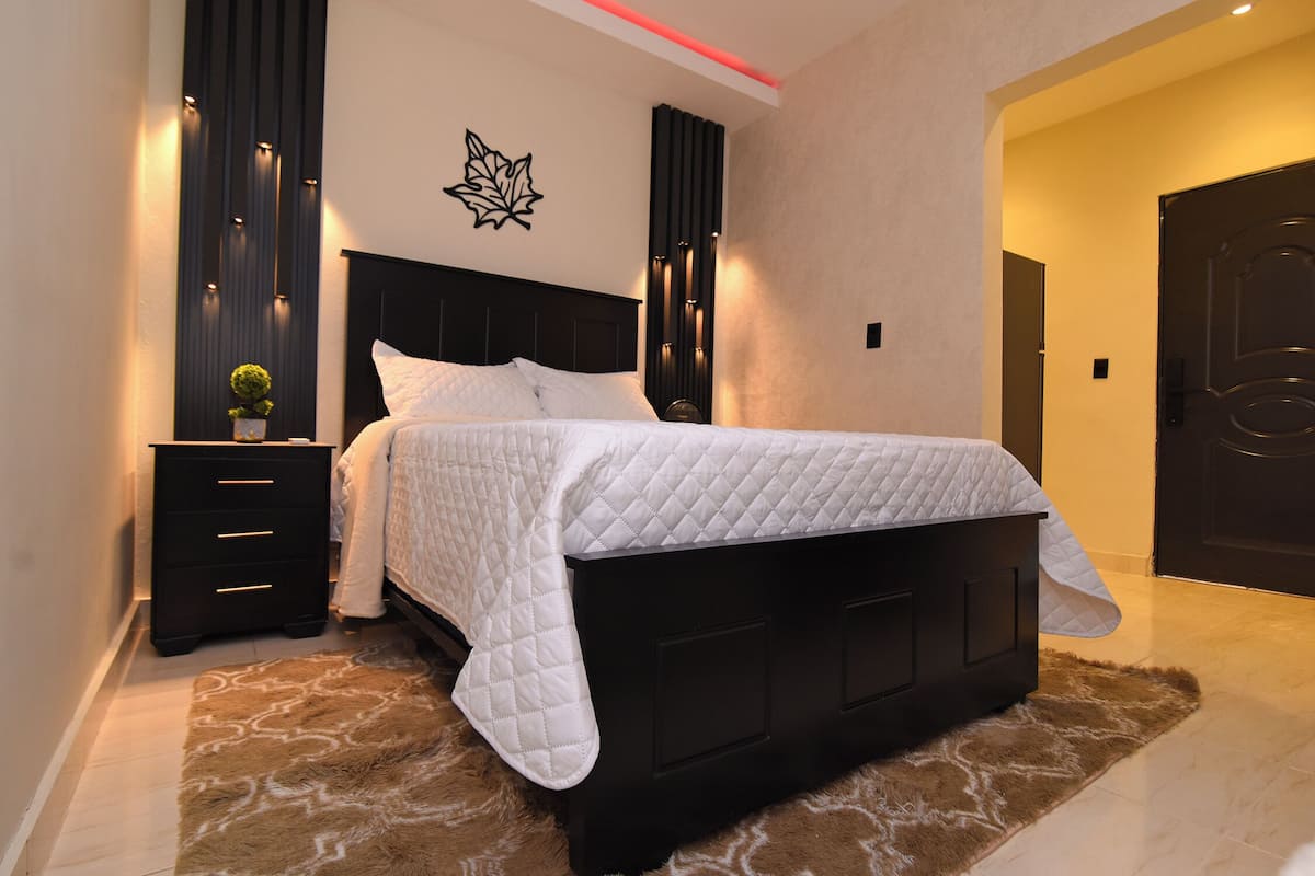 A modern bedroom with a black headboard, white bedding, and a decorative wall piece.