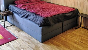 A bedroom with a large bed, wooden walls, a red abstract painting, and a wooden floor. - Green pearl vacation apartment (Nenndorf)