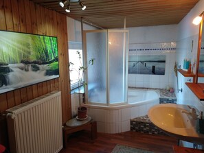 Un baño con piso de madera, una bañera, un lavamanos, una ducha y un ventanal grande.
