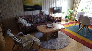 A living room with a sofa, a wooden coffee table, a rocking chair, a TV, and a colorful rug. - Green pearl vacation apartment (Nenndorf)