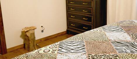Una habitación con colcha de estampado de cebra en la cama, cómoda de madera oscura, televisor montado en la pared e imagen con estampado de leopardo.