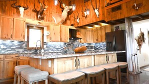 A rustic kitchen with wooden cabinets, a marble countertop, and a bar area with stools.