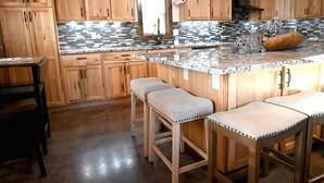 A kitchen with wooden cabinets, a granite countertop, and three bar stools.
