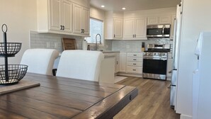 A modern kitchen with white cabinetry, stainless steel appliances, and a wooden dining table.
