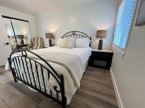Een slaapkamer met een bed, nachtkastjes, een stoel, een lamp en een raam.