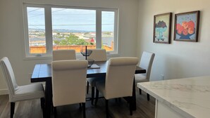 A dining area with a table and chairs, a window with a view, and two framed artworks on the wall.