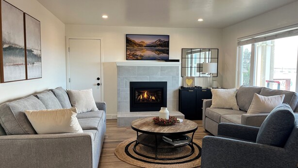 A modern living room with a fireplace, two sofas, a coffee table, and a large window.