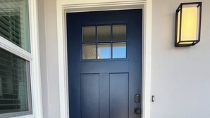 A dark blue front door with a small window above it, a doormat with "Welcome" written on it, and a wall-mounted light fixture to the right.