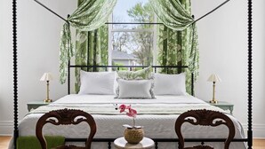 A four-poster bed with green curtains, a view of the outdoors, and a small table with a vase of flowers. - Historic Estate-Slps 16-Downtown-Soak Pool-Hot Tub (Murfreesboro)