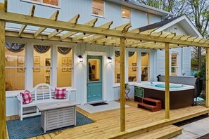 A covered patio with a wooden pergola, a hot tub, and a seating area with a bench and cushions.