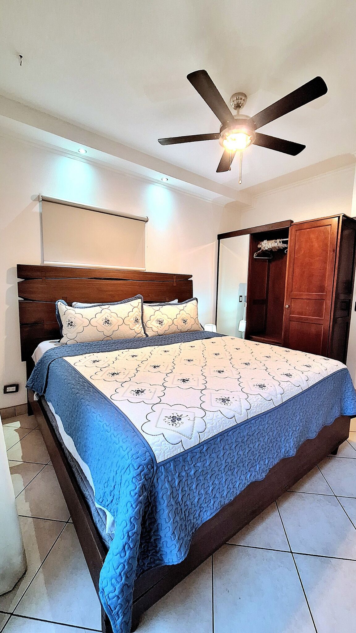 A bedroom with a bed, a ceiling fan, a wardrobe, and a door.