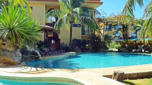 Un complexe hôtelier doté d’une grande piscine, de palmiers et d’un bâtiment avec des balcons.