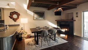 A dining area with a wooden table and chairs, a fireplace, and a kitchen with a sink and countertop. - Island Vista - Waterfront Condo (Tofino)