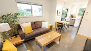 A modern living room with a brown sofa, yellow cushions, a wooden coffee table, and a dining area with a small table and chairs. - Tidal Retreat Cabin in Tofino (Tofino)