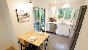 A compact kitchen with a dining area, a dishwasher, and a refrigerator. - Tidal Retreat Cabin in Tofino (Tofino)