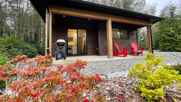 A modern house with a covered patio, a barbecue grill, and red chairs. - Tidal Retreat Cabin in Tofino (Tofino)