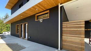 Een modern, twee verdiepingen hoog gebouw met een donkere gevel, houten lamellen aan de rechterkant en een garage deur aan de linkerkant.