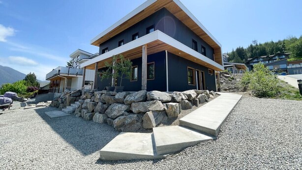 Een modern herenhuis met een stenen fundering, een houten terras en vrij uitzicht op het omliggende landschap.