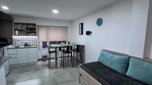 A modern kitchen with white cabinets, a dining area with a table and chairs, and a living area with a sofa. - Choconcito Suite (Ushuaia)