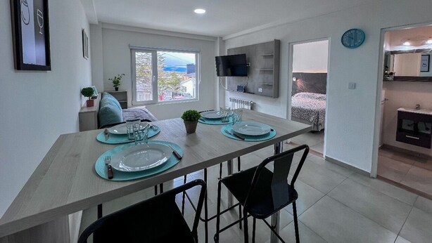 A modern kitchen with a dining area, a TV mounted on the wall, and a view of the outside. - Choconcito Suite (Ushuaia)