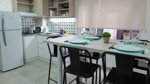 A modern kitchen with white cabinets, a white refrigerator, a microwave, and a dining table set with plates, glasses, and cutlery. - Choconcito Suite (Ushuaia)