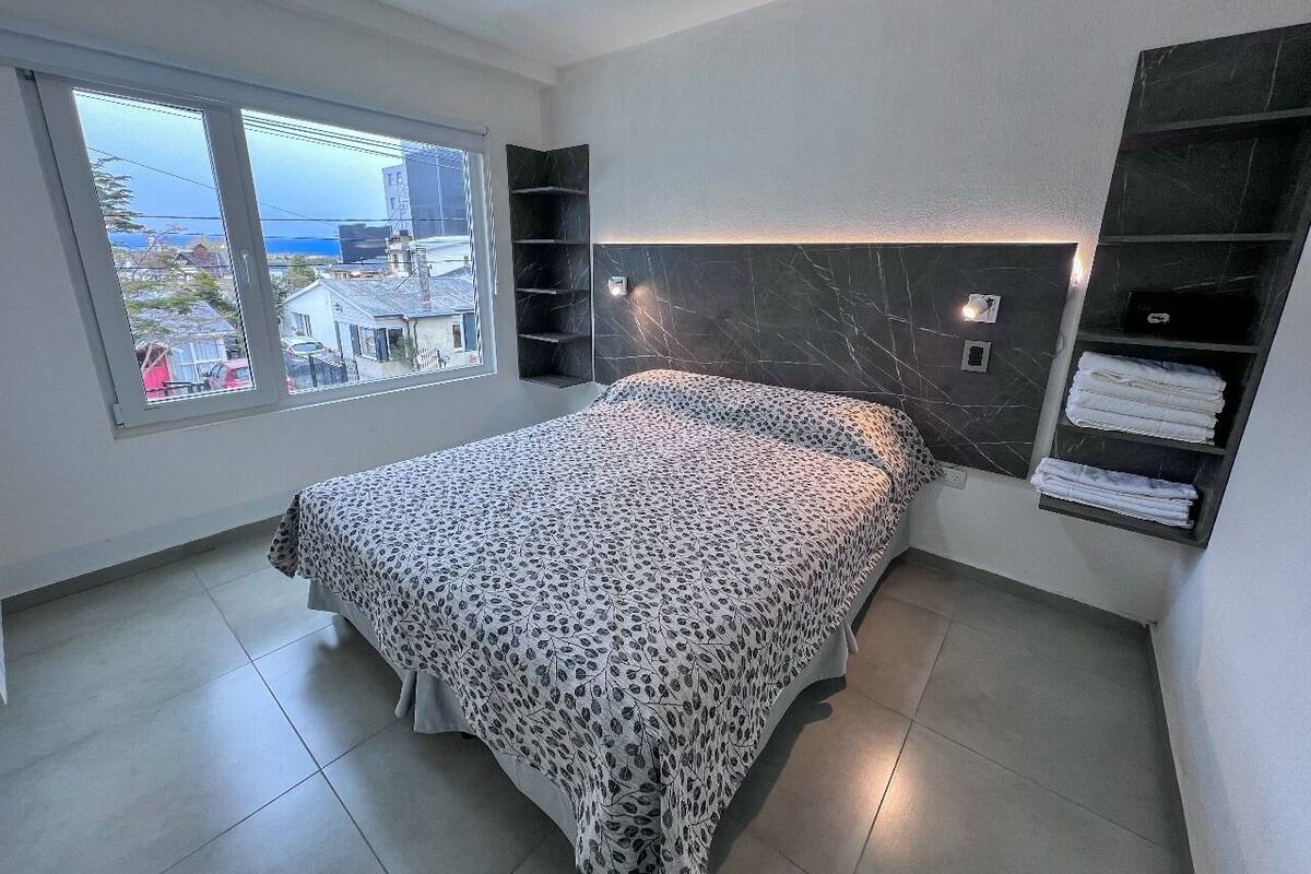 A bedroom with a bed, a window, a built-in shelf, and a view of the outside.