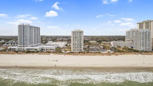 Un hôtel situé en bord de mer, composé de plusieurs immeubles de grande hauteur, avec une plage de sable fin et des vagues déferlantes.