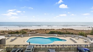 Un espace piscine avec des chaises longues et vue sur la plage.