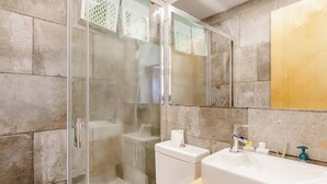 Un baño moderno con ducha acristalada, lavamanos blanco y tocador de madera.