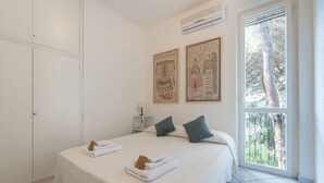 A bedroom with a bed, two pillows, a nightstand, an air conditioner, and a window with a view of trees.